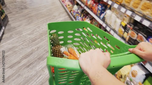Close-up view of woman moving shopping trolley with fresh colorful vegetables and fruits through aisles of supermarket, sale and shopping concept