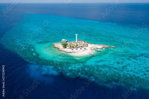 Aerial drone view of a lighthouse on a tiny tropical island surrounded by coral reef and deep water (Capitancillo Island, Cebu, Philippines)