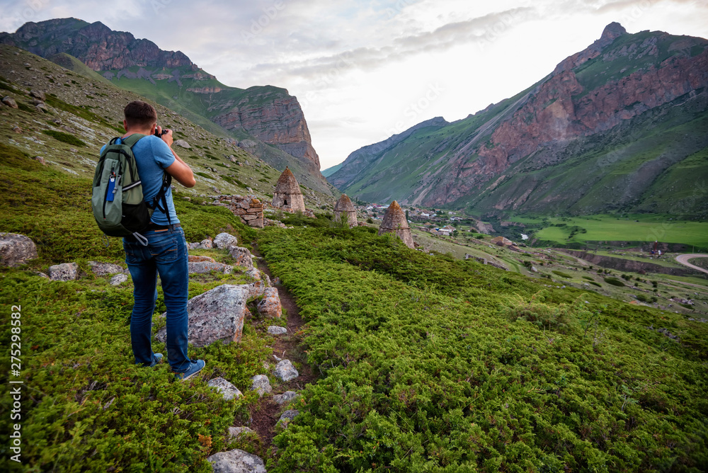 Male hiker takes photo of beautiful mountains and ancient tombs. North Caucasus