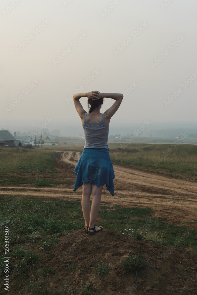 white caucasian young woman in casual clothing standing in village hill road, looking at open space, view from back in full body size, vertical lifestyle stock photo image with copy space for text white caucasian young woman in casual clothing standing in village hill road, looking at open space, view from back in full body size, vertical lifestyle stock photo image with copy space for text