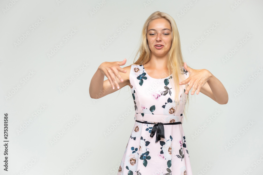 Portrait of a cute beautiful pretty woman girl with long beautiful hair on a white background in a pink dress with a pattern. Shows many different emotions, smiles and talks. Made in a studio. Portrait of a cute beautiful pretty woman girl with long beautiful hair on a white background in a pink dress with a pattern. Shows many different emotions, smiles and talks. Made in a studio.