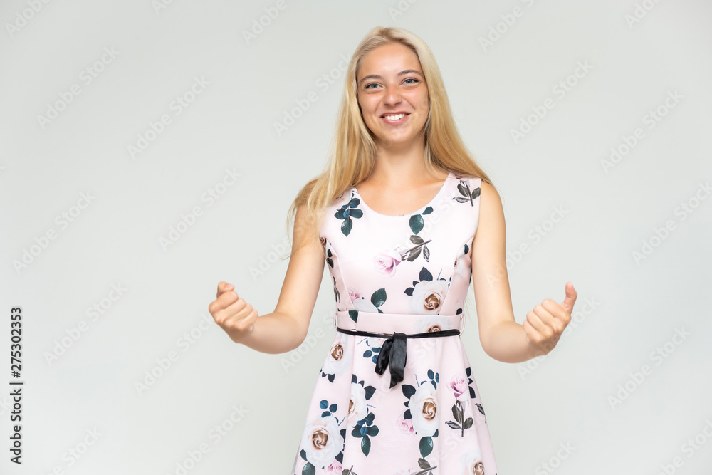 Portrait of a cute beautiful pretty woman girl with long beautiful hair on a white background in a pink dress with a pattern. Shows many different emotions, smiles and talks. Made in a studio.