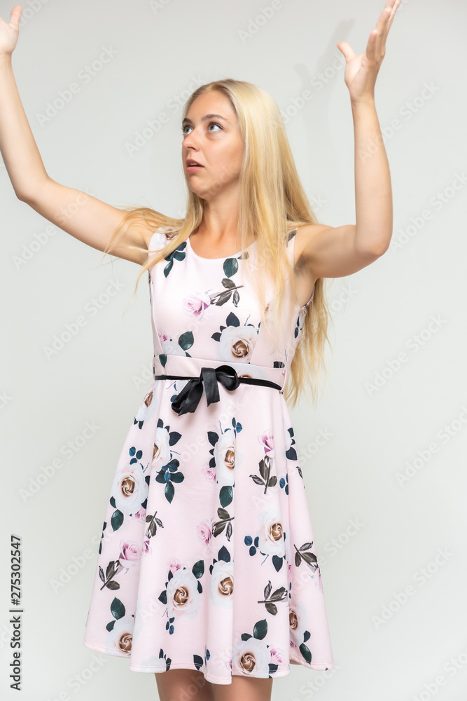 Naklejka premium Portrait of a cute beautiful pretty woman girl with long beautiful hair on a white background in a pink dress with a pattern. Shows many different emotions, smiles and talks. Made in a studio.