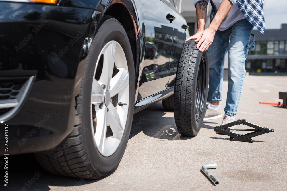 cropped view of man rolling new tire and fixing broken auto, car insurance concept cropped view of man rolling new tire and fixing broken auto, car insurance concept