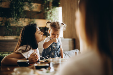 An attractive mother and her pretty girl, together with her girlfriend, rest in the cafe at the table, communicate with each other, eat and drink. beautiful woman with a child on holiday at restaurant
