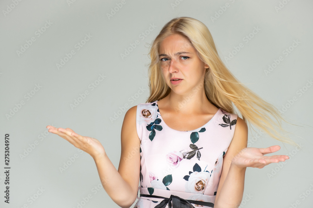 Portrait of a cute beautiful pretty woman girl with long beautiful hair on a white background in a pink dress with a pattern. Shows many different emotions, smiles and talks. Made in a studio.