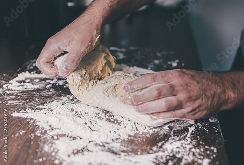 close-up of hands of man kneading yeast dough on floured kitchen counter