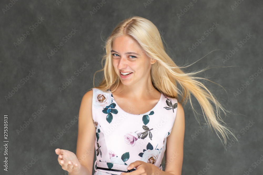 Fototapeta premium Portrait of a cute beautiful pretty woman girl with long beautiful hair on a dark gray background in a pink dress with a pattern. Shows a lot of different emotions, smiling, talking. Made in a studio.