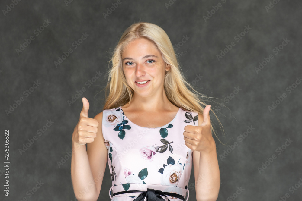 Portrait of a cute beautiful pretty woman girl with long beautiful hair on a dark gray background in a pink dress with a pattern. Shows a lot of different emotions, smiling, talking. Made in a studio. Portrait of a cute beautiful pretty woman girl with long beautiful hair on a dark gray background in a pink dress with a pattern. Shows a lot of different emotions, smiling, talking. Made in a studio.