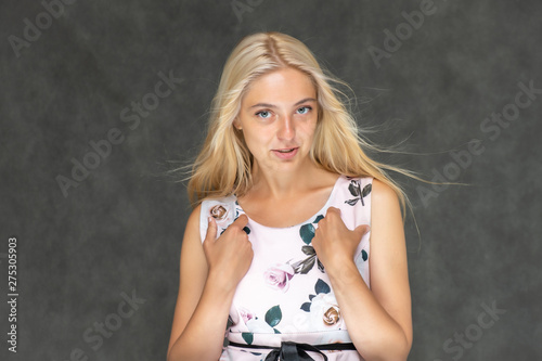 Portrait of a cute beautiful pretty woman girl with long beautiful hair on a dark gray background in a pink dress with a pattern. Shows a lot of different emotions, smiling, talking. Made in a studio.