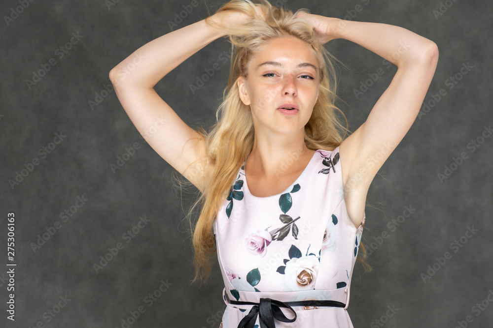 Portrait of a cute beautiful pretty woman girl with long beautiful hair on a dark gray background in a pink dress with a pattern. Shows a lot of different emotions, smiling, talking. Made in a studio.