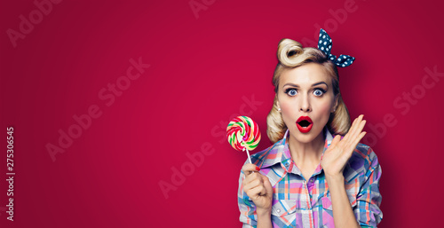 Photo of beautiful very surprised woman with lollipop, in pinup style, over dark red color background