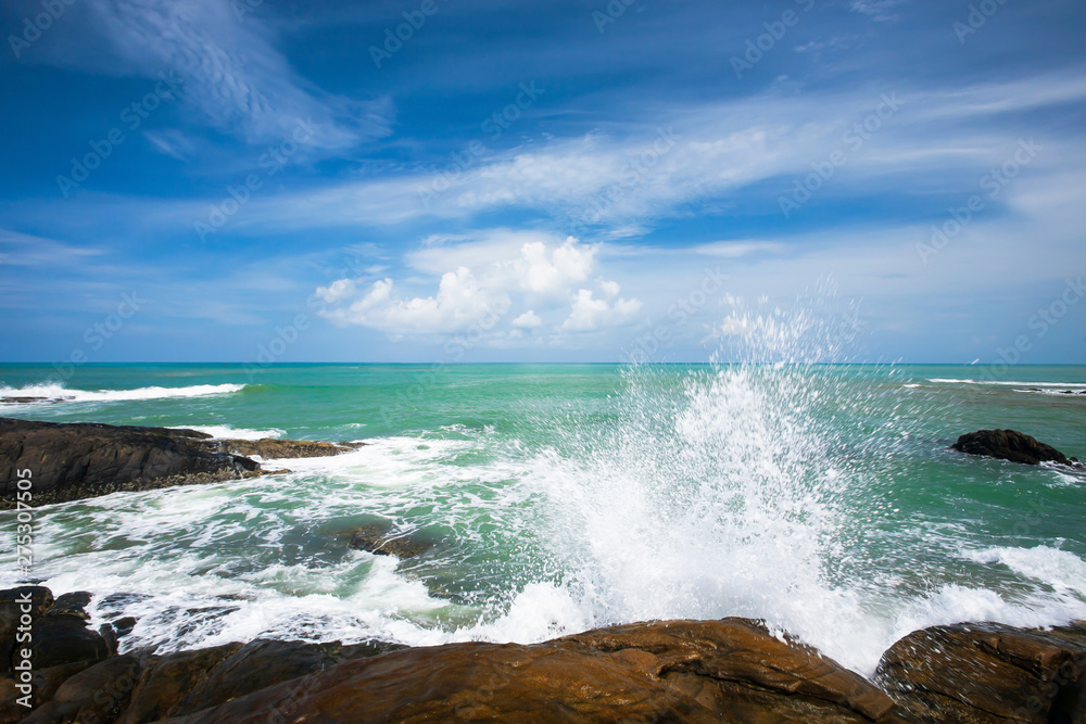 Relaxing ocean waves crashing into rocky shore on sunny summer.