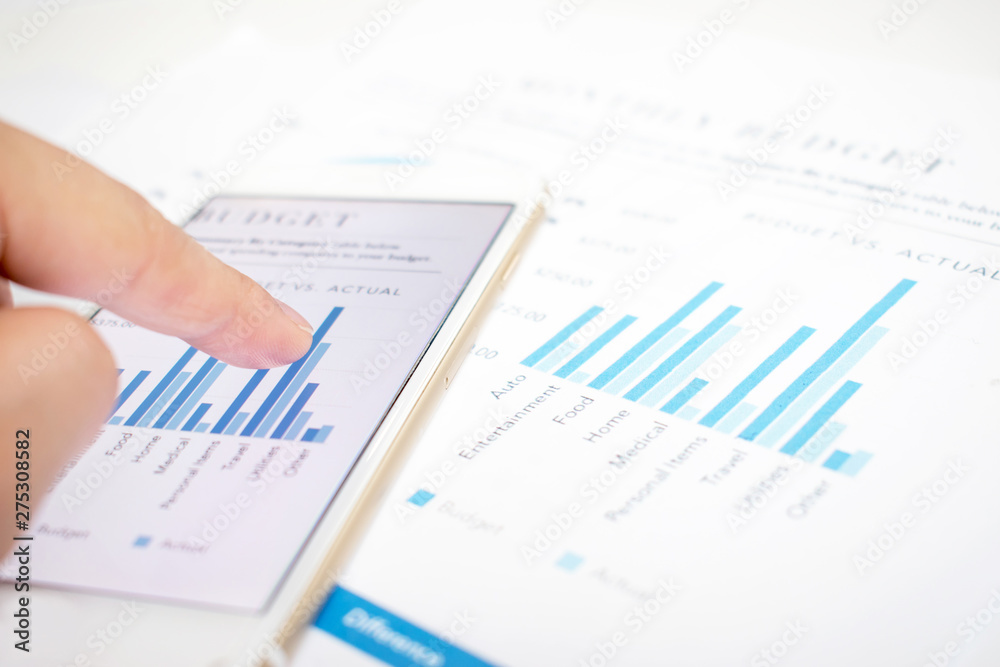 Close-up pictures of businessmen pointing to the smartphone screen showing some graphs. Modern white desk with financial documents. Close-up pictures of businessmen pointing to the smartphone screen showing some graphs. Modern white desk with financial documents.