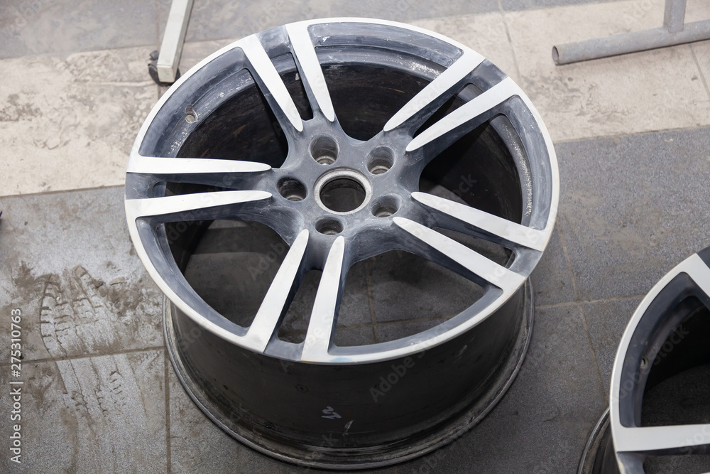 Preparing the surface of the aluminum wheel of the car for subsequent painting in the workshop, cleaning and leveling the wheel with the help of abrasive material. Auto service industry.