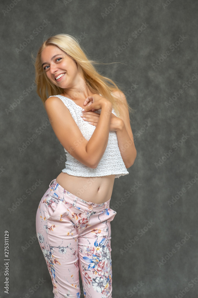 Portrait of a cute beautiful pretty woman girl with long beautiful hair on a dark gray background in pink trousers with a pattern. Shows many different emotions, smiles and talks. Made in a studio. Portrait of a cute beautiful pretty woman girl with long beautiful hair on a dark gray background in pink trousers with a pattern. Shows many different emotions, smiles and talks. Made in a studio.