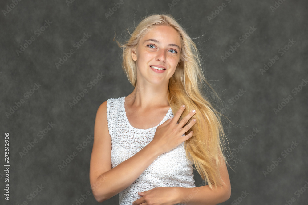 Naklejka premium Portrait of a cute beautiful pretty woman girl with long beautiful hair on a dark gray background in a white sweater with a pattern. Shows many different emotions, smiles and talks. Made in a studio.