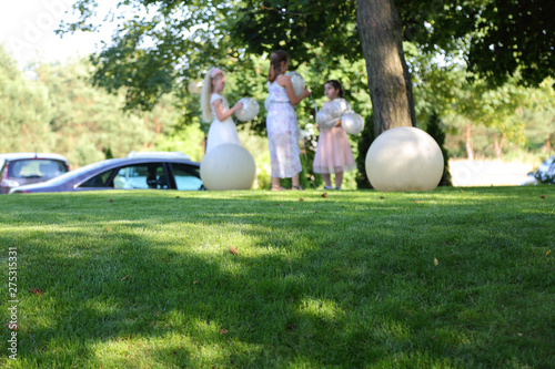 Dziewczynki z balonami na wzniesieniu pokrytym zieloną trawą.
