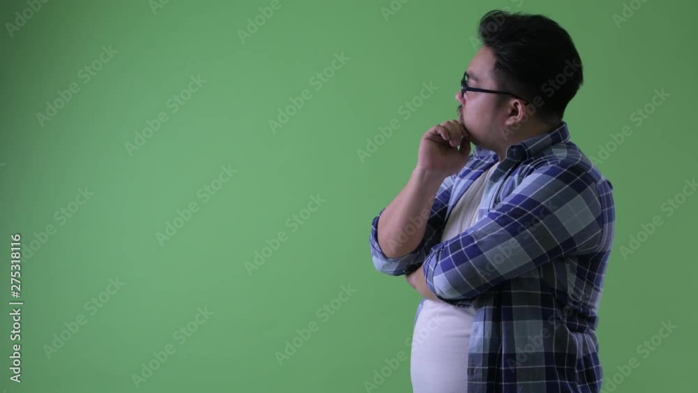 Profile view of happy young overweight Asian hipster man thinking Profile view of happy young overweight Asian hipster man thinking