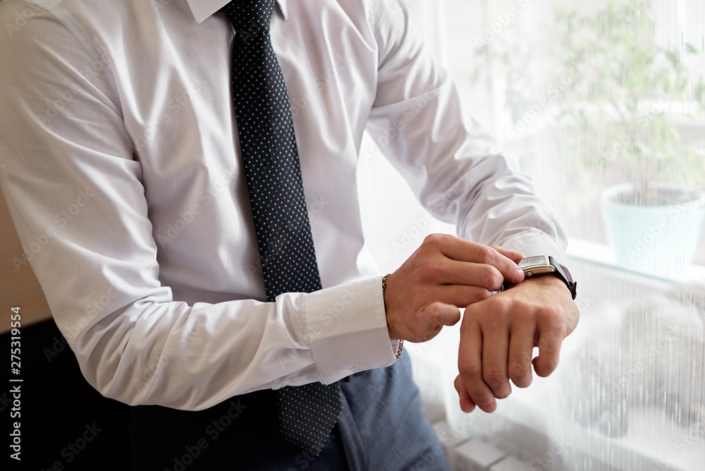 Obraz premium Businessman looking at watches on his hand indoors, free space. Man in white shirt checking time from luxury wristwatches. Watch on hand. Groom wedding preparation