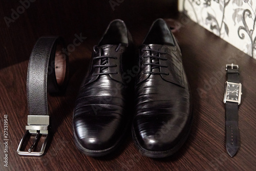 Close up of black male shoes, belt and watches on wood table background, copy space. Modern man accessories. Wedding details. Male casual outfits