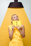 positive woman holding notebook while posing on white and yellow