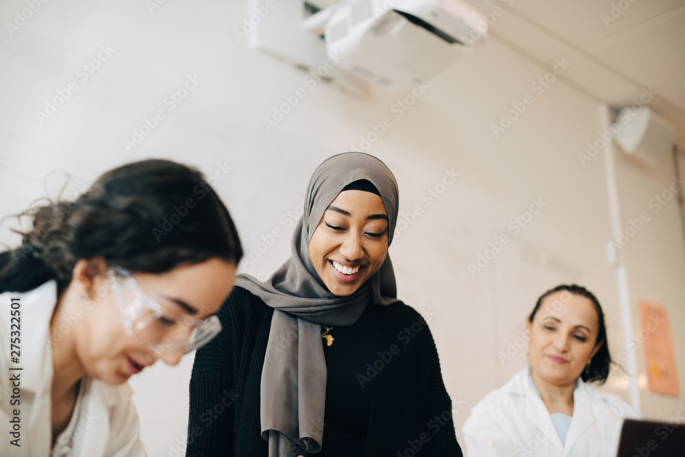 Fototapeta premium Teacher looking at smiling teenage girls experimenting during science class
