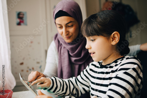 Canvas Print Girl sitting with mother learning homework from digital tablet at home