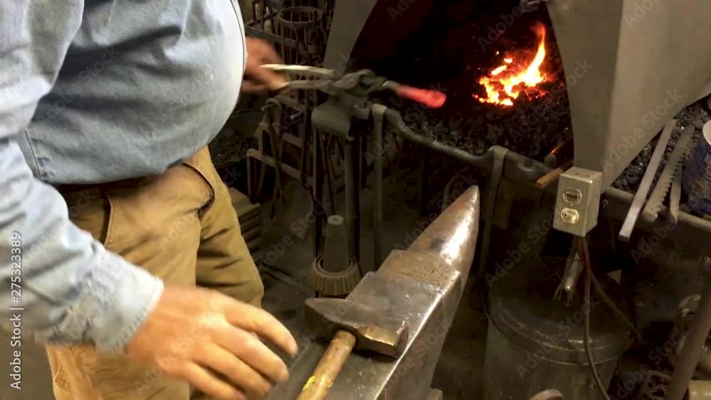 Blacksmith hammers bends metal anvil
