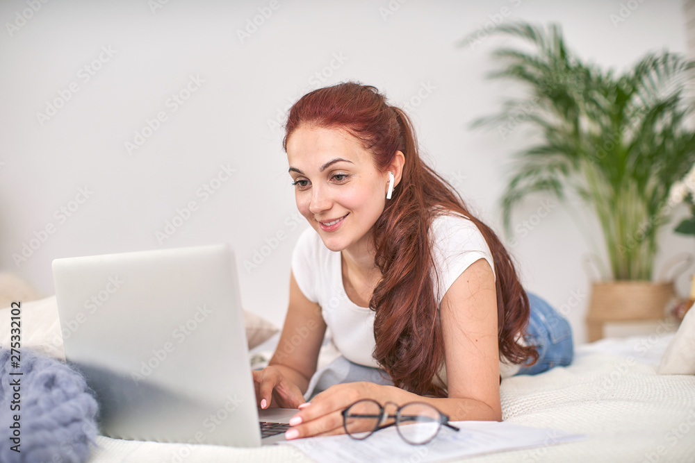 the student is happy to communicate with friends via the Internet. home schooling, work and study, new knowledge.happy teen on bed with computer. girl student lying on the bed smiling. the student is happy to communicate with friends via the Internet. home schooling, work and study, new knowledge.happy teen on bed with computer. girl student lying on the bed smiling.