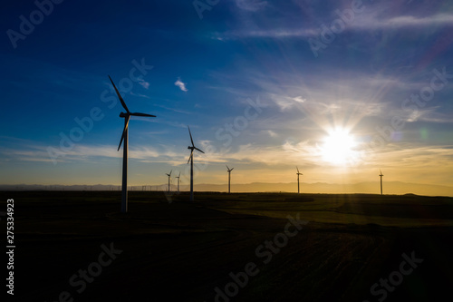 Silhouette Modern windmills with propellers standing in rural farmland agri meadow over orange sunset sky. Wind blowing generating renewable energy for clean resources. Electric power production © BullRun