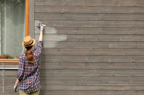 Fototapeta Naklejka Na Ścianę i Meble -  Woman worker painting wooden house exterior wall with paintbrush and wood protective color
