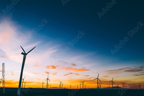 Silhouette of windmills station with propellers generating alternative clean green power from eco resources in rural agri environment against blue sunset sky. Farm of turbines producing electricity photo