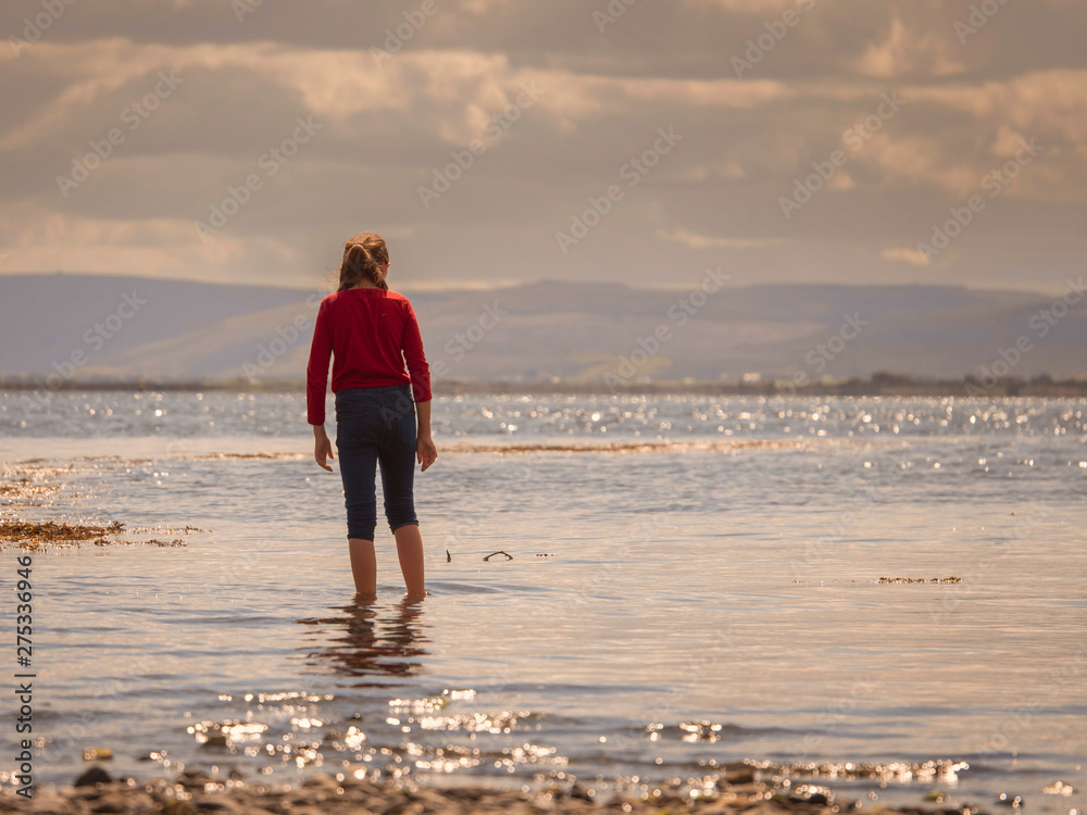 Girl walking in ocean's water, cloudy sky, Connemara national park. Ireland. Warm colors.