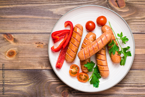 Grilled sausages, fresh tomatoes, peppers and parsley on a plate on a wooden table. Top view. Copy space