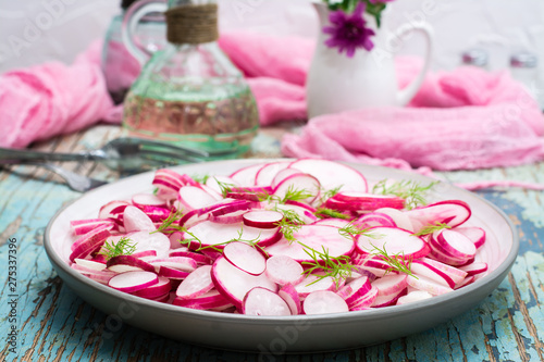 Fresh salad of pieces of radish and dill on a plate on a wooden table. Ready snack for a diet