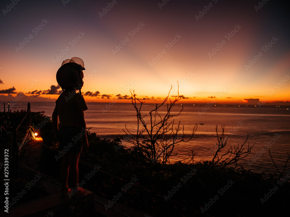 A boy in a helmet looks at the sunset at sea on the viewpoint A boy in a helmet looks at the sunset at sea on the viewpoint