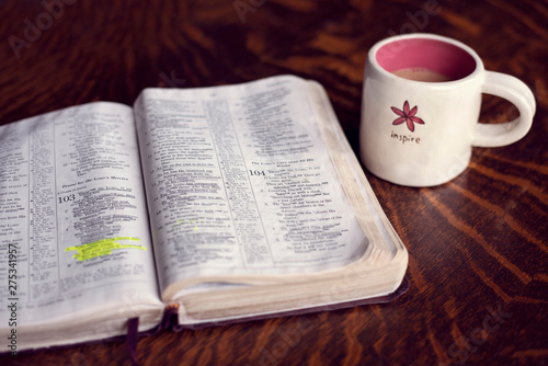 An open Bible with a pink inspiring coffee mug on a wooden coffee table