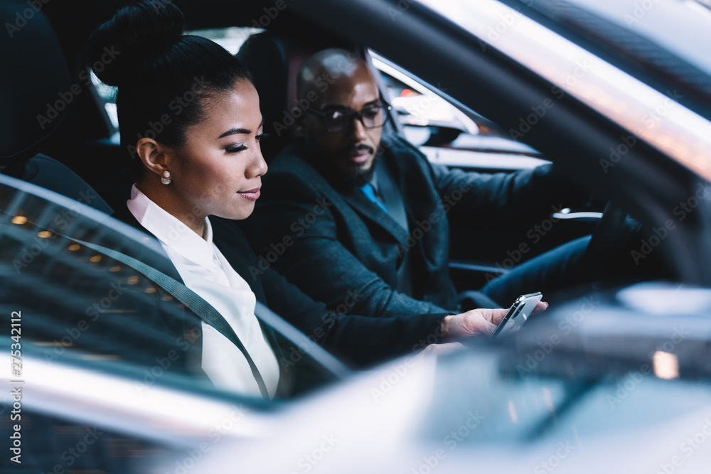 Male and female experienced lawyers in formal wear tracking gps via cellphone application while driving in car connected to 4g wireless for browsing internet, serious colleagues using smartphone