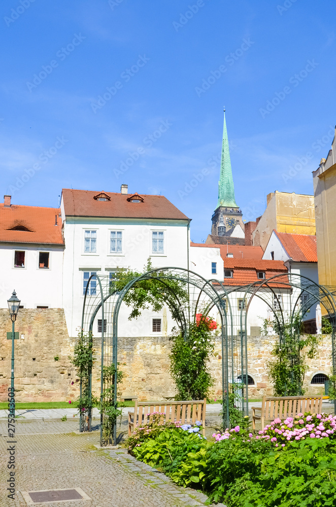 Beautiful buildings in the old town of Plzen, Czech Republic with dominant Cathedral of St. Bartholomew shot from adjacent park. Pilsen, Western Bohemia, Czechia. Sunny day, blue sky