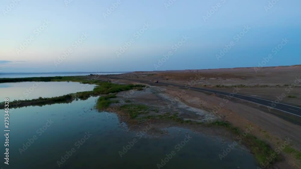 Aerial view of car driving during sunset on an empty road in the middle of the desert next The Ailik  or Aylik lake in Xinjiang Uighur Autonomous Region of China.
