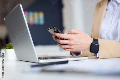 Mid age businesswoman making notes on the phone sitting at laptop in the office