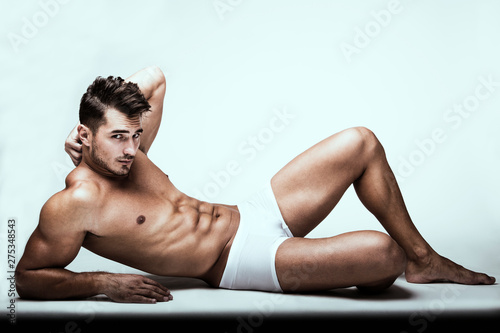 Portrait of handsome young man with stylish haircut in white underwear posing over white background. Perfect hair & skin. Close up. Studio shot