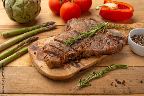 Marbled beef steak on a board with rosemary pepper, seasoning, and fresh vegetables on a wooden background, restaurant menu, gastronomy, tasty food. Restaurant service