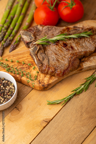 Marbled beef steak on a board with rosemary pepper, seasoning, and fresh vegetables on a wooden background, restaurant menu, gastronomy, tasty food. Restaurant service, verikalnoe photo, banner photo