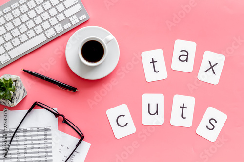 Tax cuts copy on accountant work place with keyboard, coffee and glass on pink desk background top view