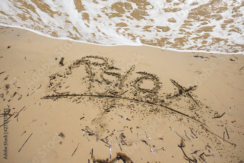 Summer holiday concept with relax word handwritten on the beach, in front of the waves