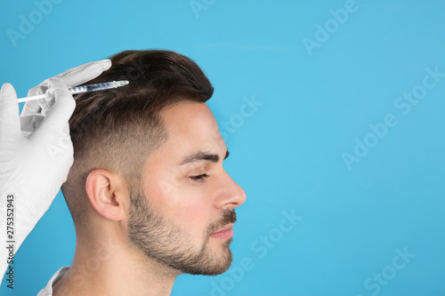 Young man with hair loss problem receiving injection on color background. Space for text