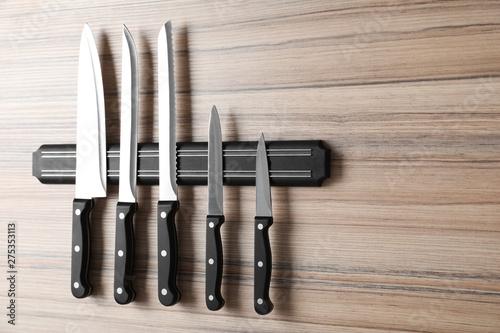 Magnetic holder with set of knives on wooden background. Space for text