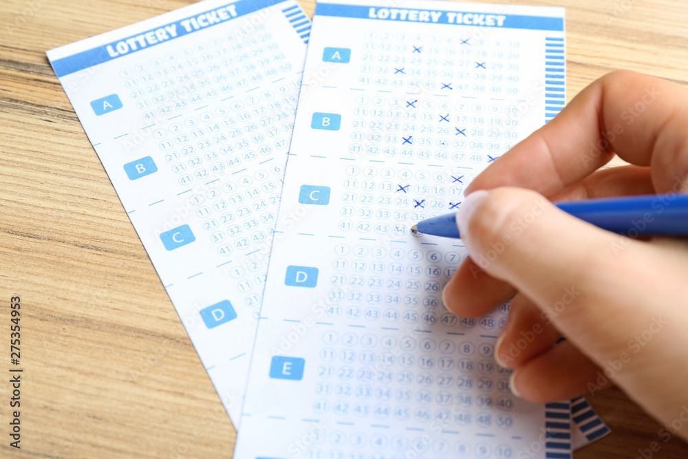 Woman filling out lottery tickets with pen on wooden table, closeup. Space for text Woman filling out lottery tickets with pen on wooden table, closeup. Space for text